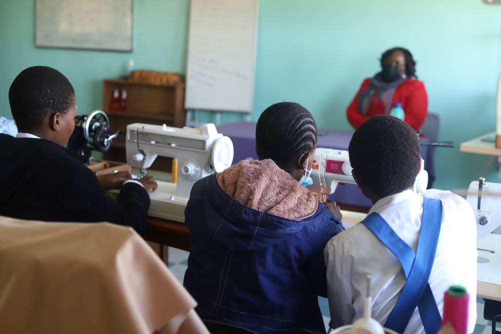 3 young women, backs to the camera, in a sewing class