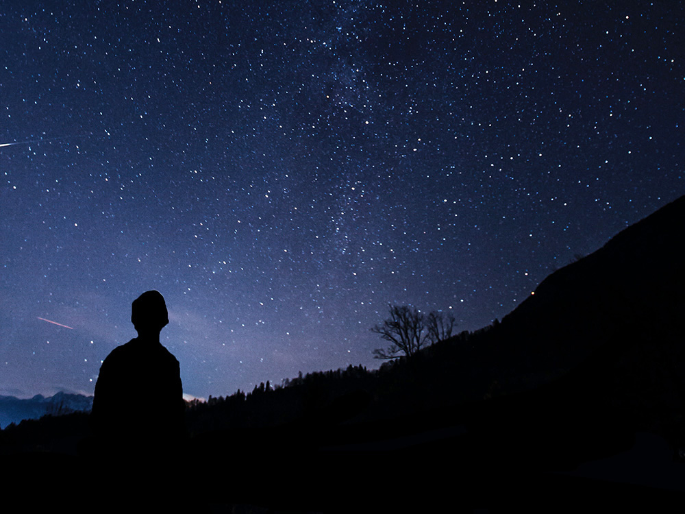 A landscape with a person looking at the stars (Unsplash/Klemen Vrankar)