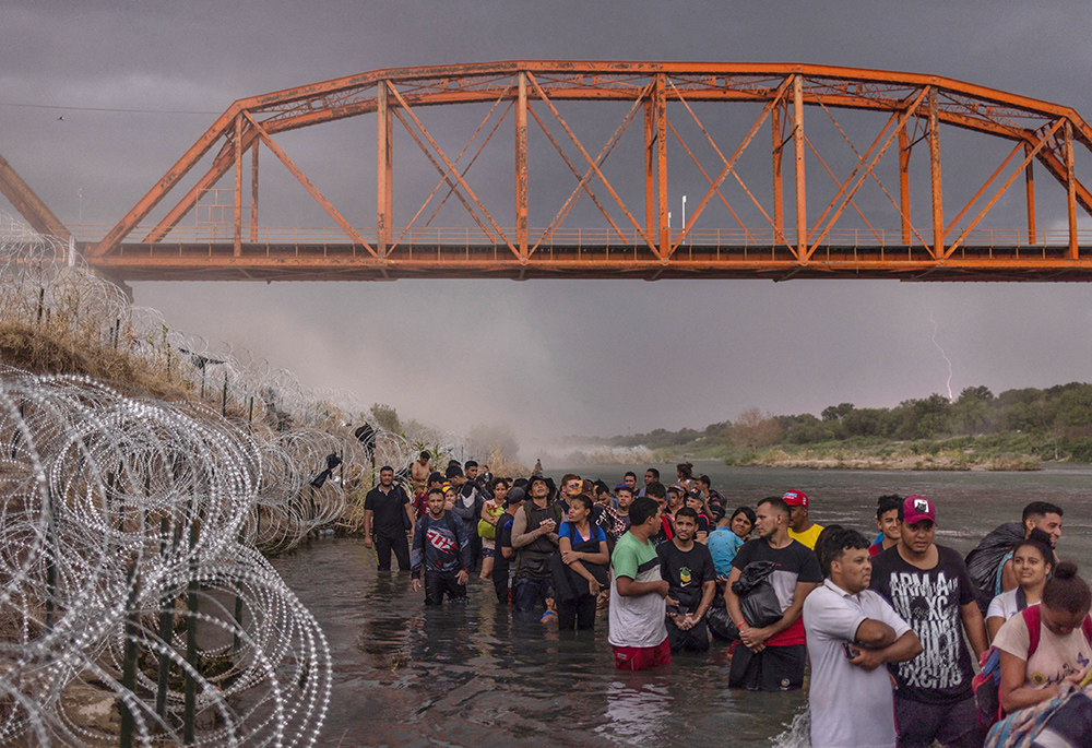 Lightning strikes and dust blows in the background from an incoming thunderstorm Sept. 15 as hundreds of migrants line up under the Puente Negro Ferrocarril train bridge and wait to surrender to authorities after wading across the Rio Grande from Mexico to enter the United States at Eagle Pass, Texas. (OSV News/Reuters/Adrees Latif)