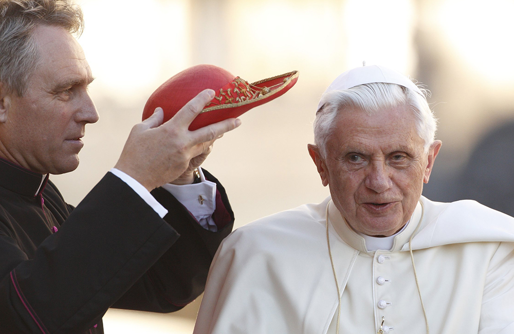 Then-Msgr. Georg Ganswein places a red hat on Pope Benedict XVI as the pope arrives to lead his general audience in St. Peter's Square at the Vatican in this Oct. 6, 2010, file photo. (CNS/Paul Haring)
