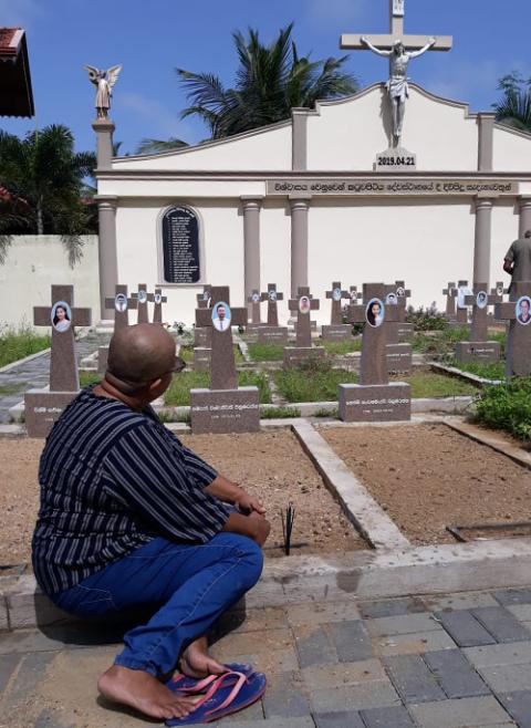 Niranjalee Yasawaradana, a widow who lost her husband and two daughters in the 2019 Easter bombing, prays before their crosses on her Saturday weekly visit to the mass burial grounds at St. Sebastian's parish church in Negombo, Sri Lanka. (Courtesy of Niranjalee Yasawaradana)