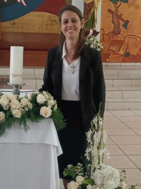 Scalabrinian Sister Nyzelle Dondé, standing next to the altar, where white flowers and a white candle rest. 