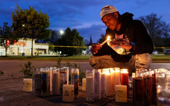 A man at a Tops supermarket in Buffalo, New York, lights a candle May 16 for the victims of a May 14 mass shooting that authorities said was motivated by racism. (CNS/Reuters/Brendan McDermid)