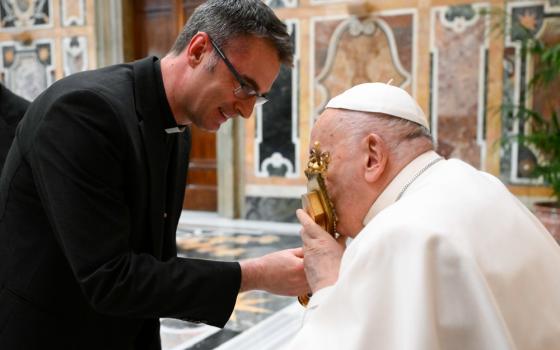 Pope Francis kisses a gold reliquary while seated. 