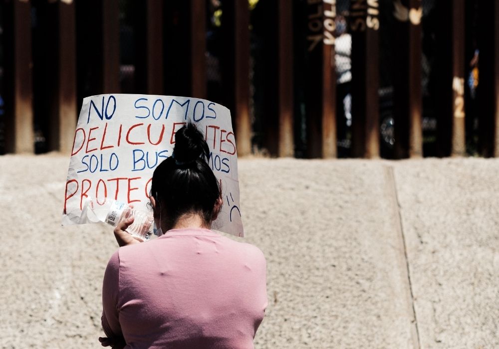 A woman holds a poster at an Aug. 6 border wall encounter at the U.S.-Mexico border, which was organized by the Save Asylum coalition to protest the dismantling of the asylum process. Kino Border Initiative is one of the coalition's supporting organizatio