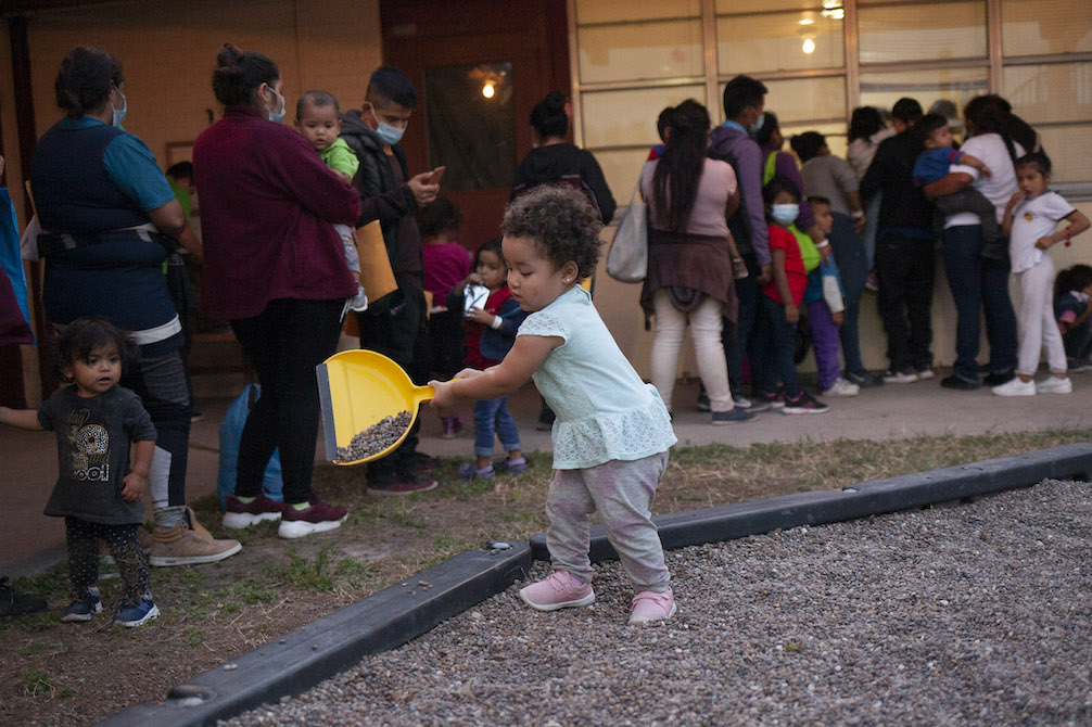 Toddler plays with a dustpan and gravel while others wait in a line