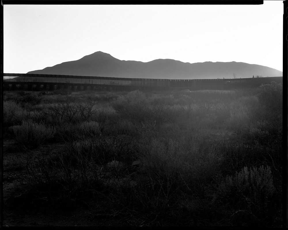 Twilight in Naco, Arizona, extends a haze against its border wall, a "scar on the landscape," as Elmaleh saw it: "Beautiful mountains, vast desert, difficult to cross, and then this massive 30-foot wall is part of the landscape." (© Lisa Elmaleh)