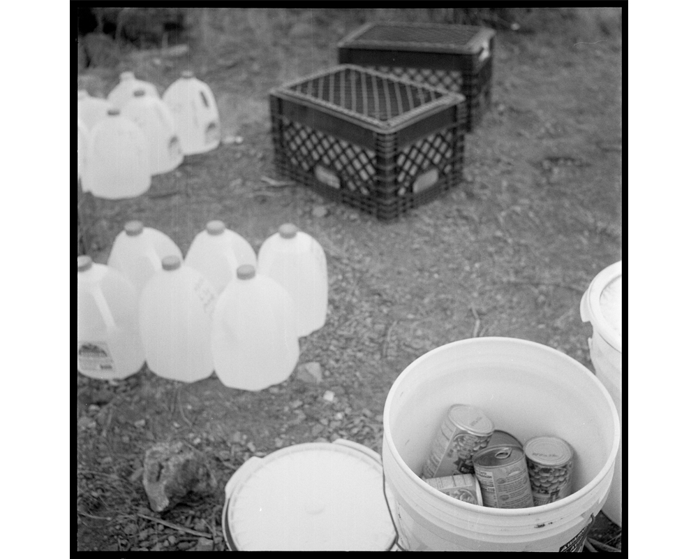 Water bottles are lined up and food is placed in buckets. Jugs are placed under milk crates to prevent animal damage to the bottles. In deciding how much to leave and where, the Samaritans base decisions on the data they record from the migrants' use of w