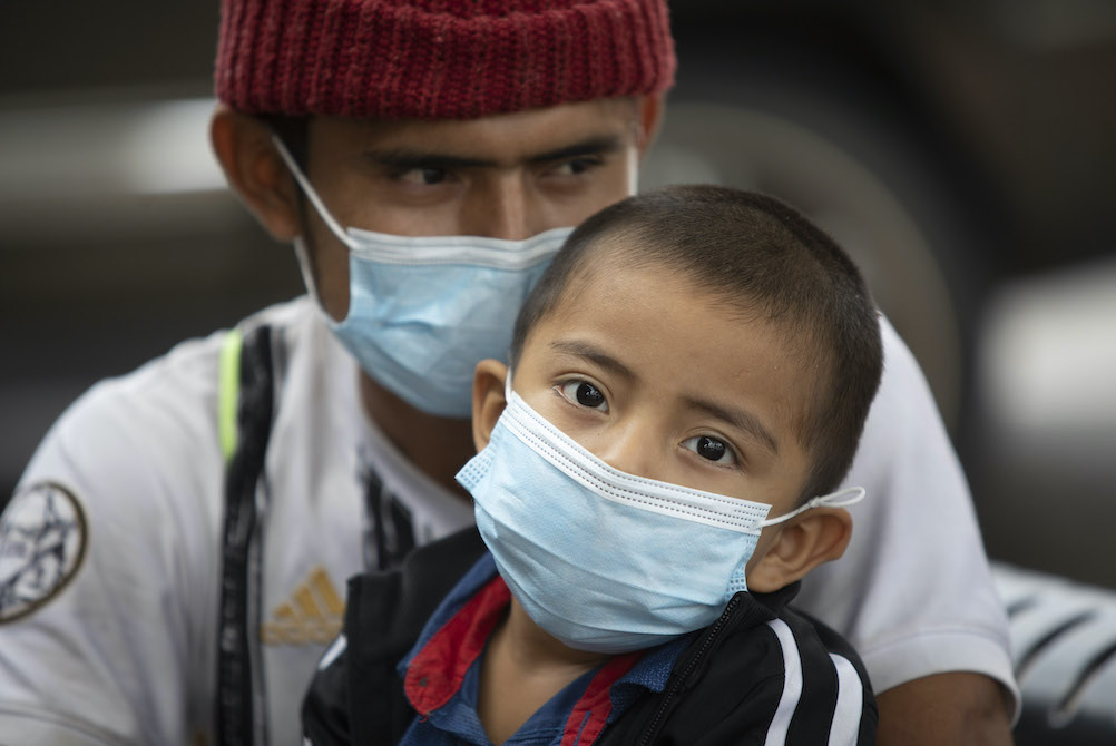 A young boy in a mask, held by his father in a mask