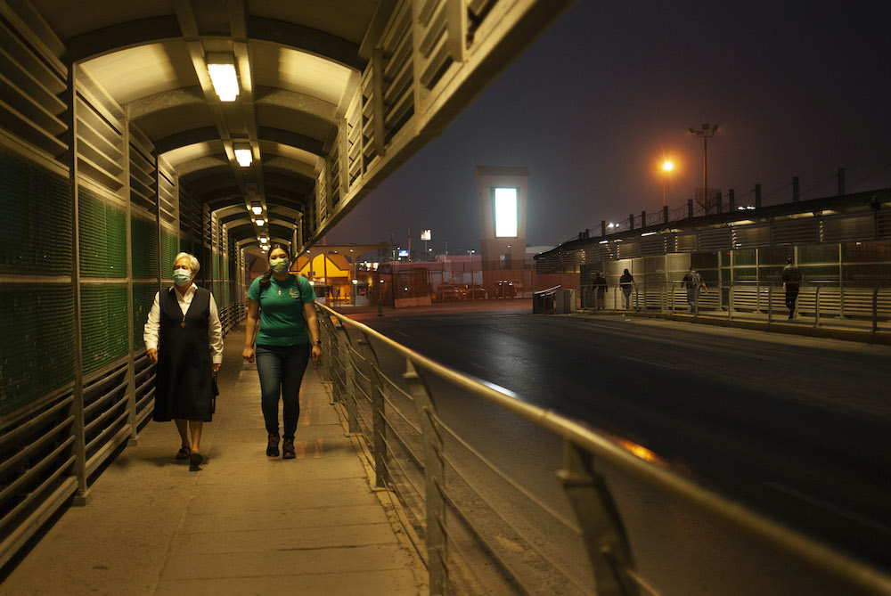 Catholic sister and younger woman walk toward camera along bridge