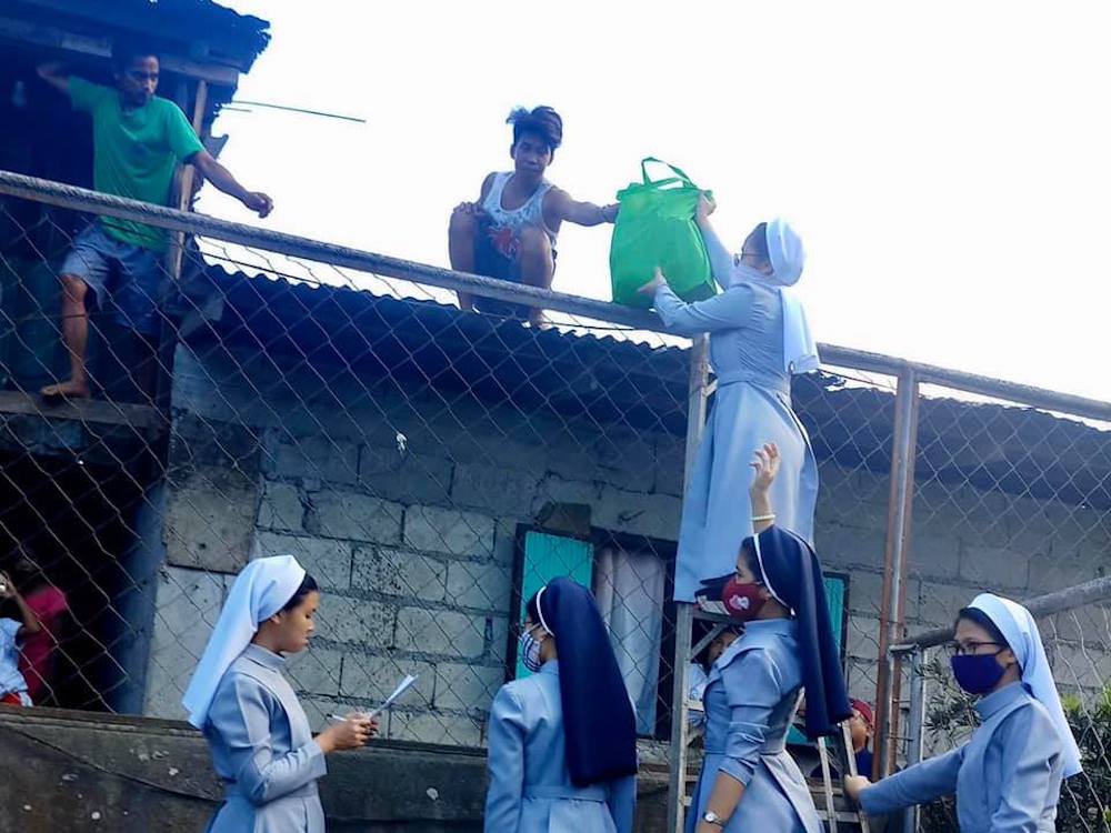 Catholic sisters in the Philippines hand bags of food over a fence to day laborers