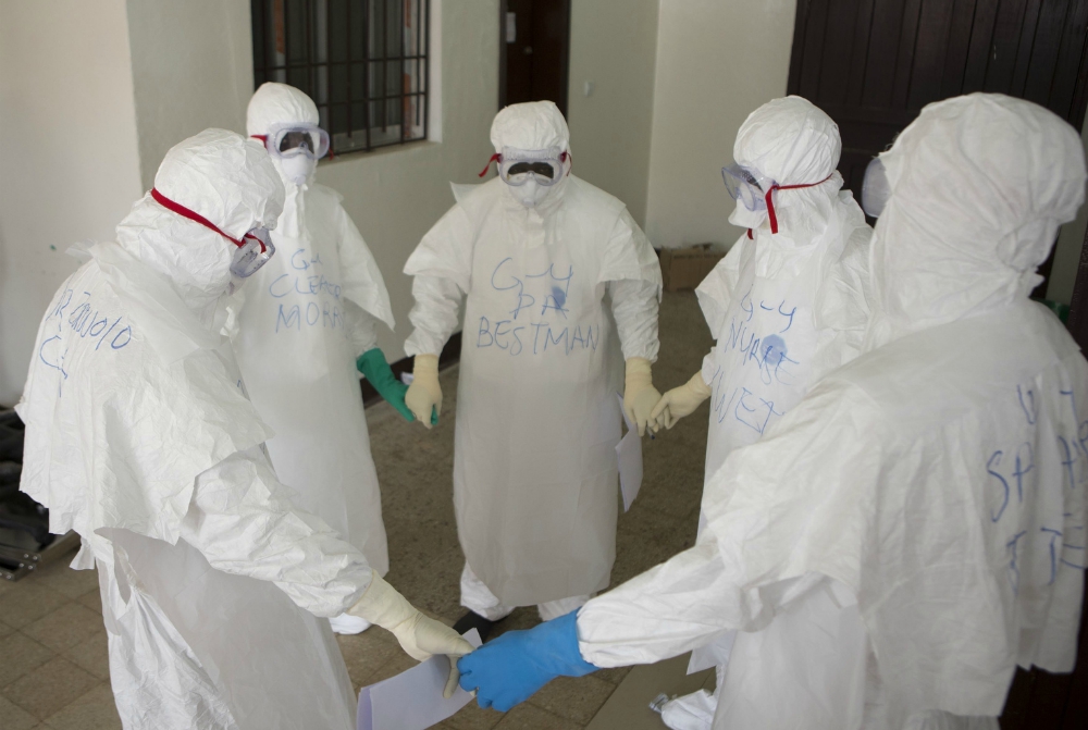 Health workers wearing protective equipment pray at the start of their shift at an Ebola treatment center in Monrovia, Liberia, on Sept. 30, 2014. (CNS / WHO / Christopher Black, handout via Reuters)