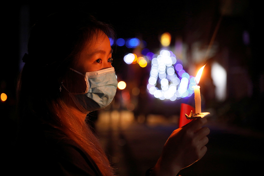 A woman wearing a protective face mask holds a candle in her home while watching Easter Mass via livestream near Hanoi, Vietnam, April 12, 2020, during the COVID-19 pandemic. (CNS/Reuters/Kham)