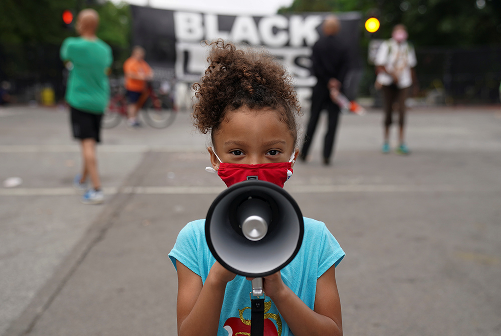 Mischa, 6, from Maryland, holds a bullhorn in front of a "Black Lives Matter" protest sign near the White House June 10, 2020, in Washington. (CNS/Kevin Lamarque, Reuters)