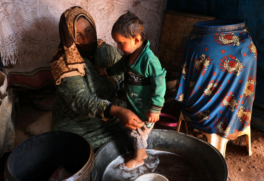 Fawza Umri helps her son put on clothes after being bathed inside their tent at Atmeh refugee camp, near the Turkish border in Syria, on June 13. (CNS/Reuters/Khalil Ashawi)