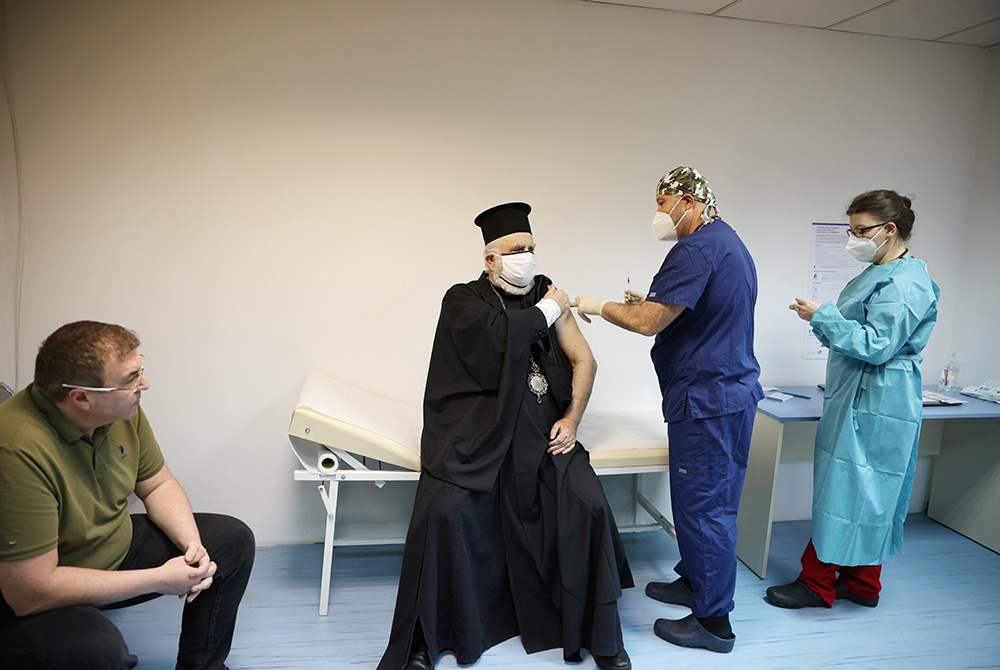 Bulgarian Health Minister Kostadin Angelov watches an Orthodox priest receive the Pfizer-BioNTech coronavirus vaccine Dec. 27 at St. Anna Hospital in Sofia, Bulgaria. (CNS/Reuters/Stoyan Nenov)