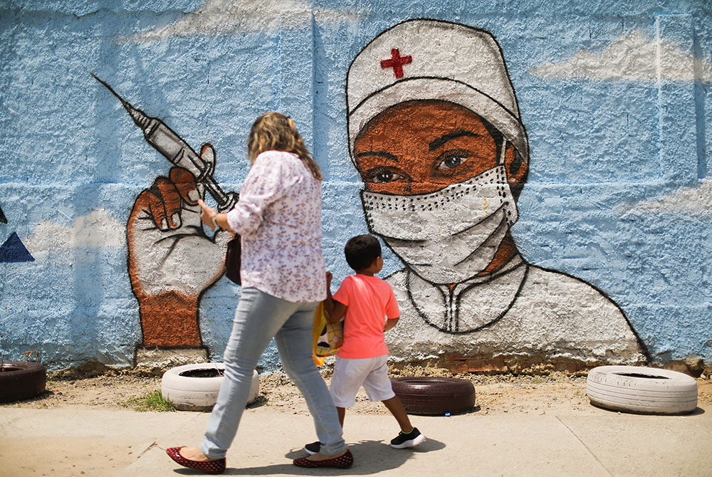 A woman and child walk past a painting on a wall March 12 in Rio de Janeiro during the COVID-19 pandemic. (CNS/Reuters/Pilar Olivares)
