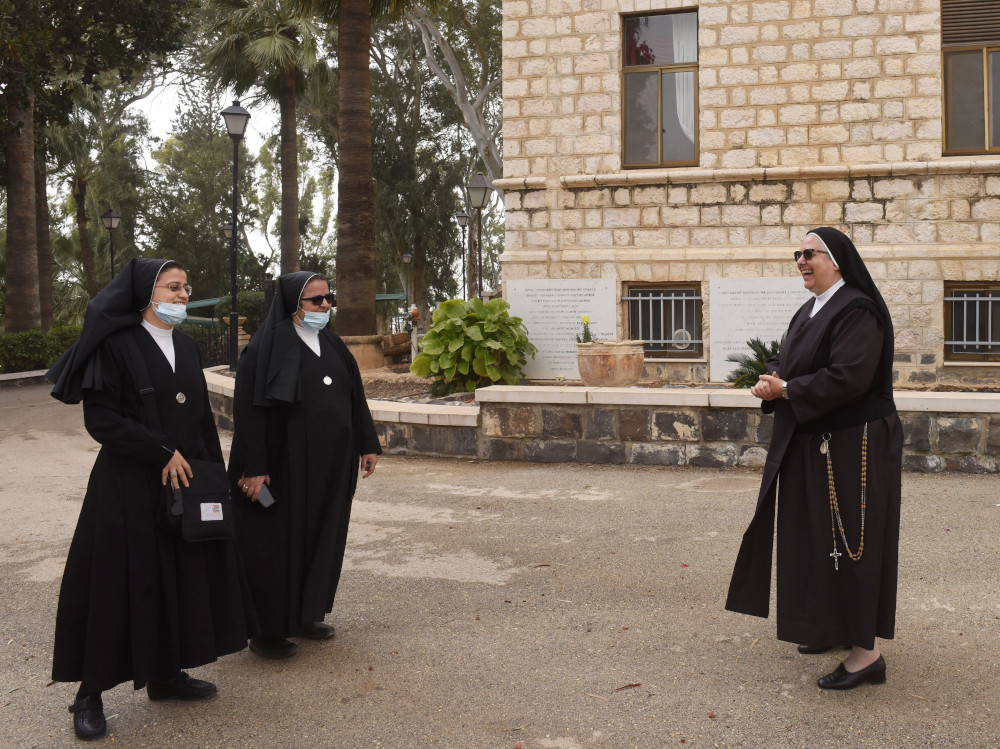 Three nuns in habits meet outside of a stone building