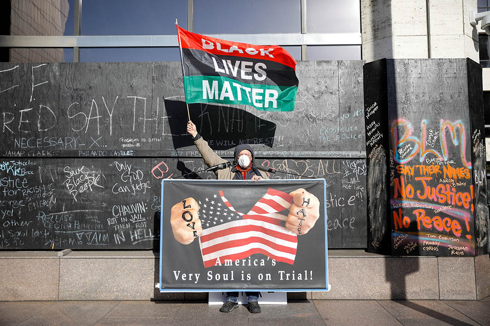 A demonstrator holds a Black Lives Matter flag and another sign April 6 outside the Hennepin County Government Center in Minneapolis on the seventh day of the trial of former police officer Derek Chauvin. (CNS/Reuters/Nicholas Pfosi)