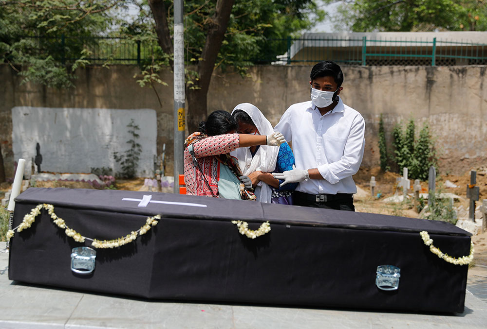 Relatives of a person who died after contracting COVID-19 mourn April 29 over the casket before the burial at a graveyard in New Delhi. (CNS/Reuters/Adnan Abidi)