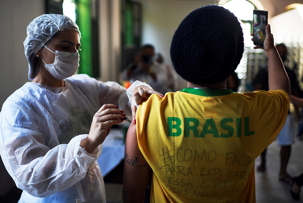 A health care worker administers a dose of the Johnson & Johnson COVID-19 vaccine to a resident taking a selfie in Rio de Janeiro on July 10. (CNS/Reuters/Lucas Landau)