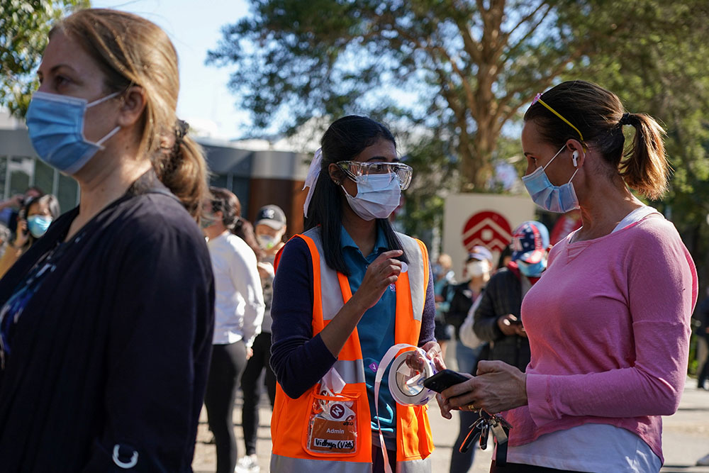 A staff member assists people waiting in line outside a COVID-19 vaccination center at Sydney Olympic Park during a lockdown to curb the spread of an outbreak in Sydney Aug. 16. (CNS/Reuters/Loren Elliott)