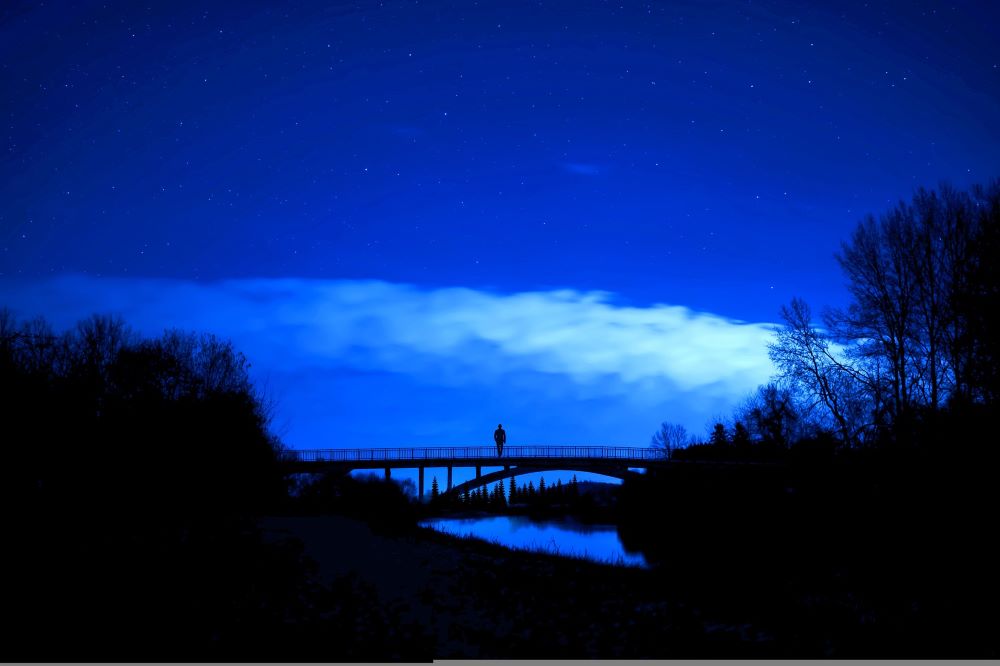 a person stands alone in the center of a bridge at night 