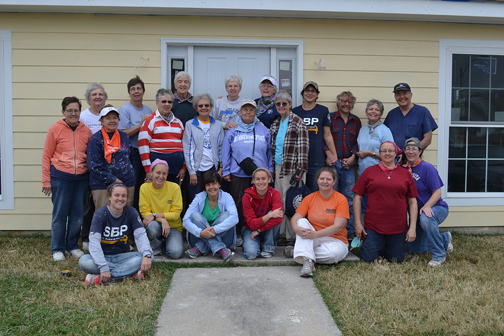 A group of people poses for a photo outside of a yellow house