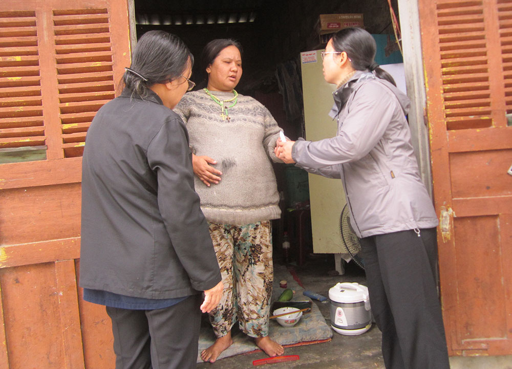 Daughters of Our Lady of the Visitation Srs. Lucia Nguyen Thi Hong (right) and Mary Le Thi Thu Huong talk with Cecilia Nguyen Thi Thu Thanh, a kidney patient, at her rented room in An Cuu ward in Hue, Vietnam, Aug. 6. (GSR photo/Joachim Pham)