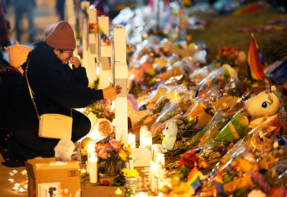 A woman in a black coat and knit hat cries as she knees next to a makeshift memorial during a candlelight vigil