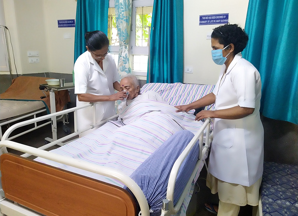 Holy Cross Sr. Daya Mathew feeds a bedridden patient with the help of Holy Cross Sr. Nitya Pausthin at Shanti Avedna Sadan, a hospice for terminally ill cancer patients, in New Delhi. (Jessy Joseph)