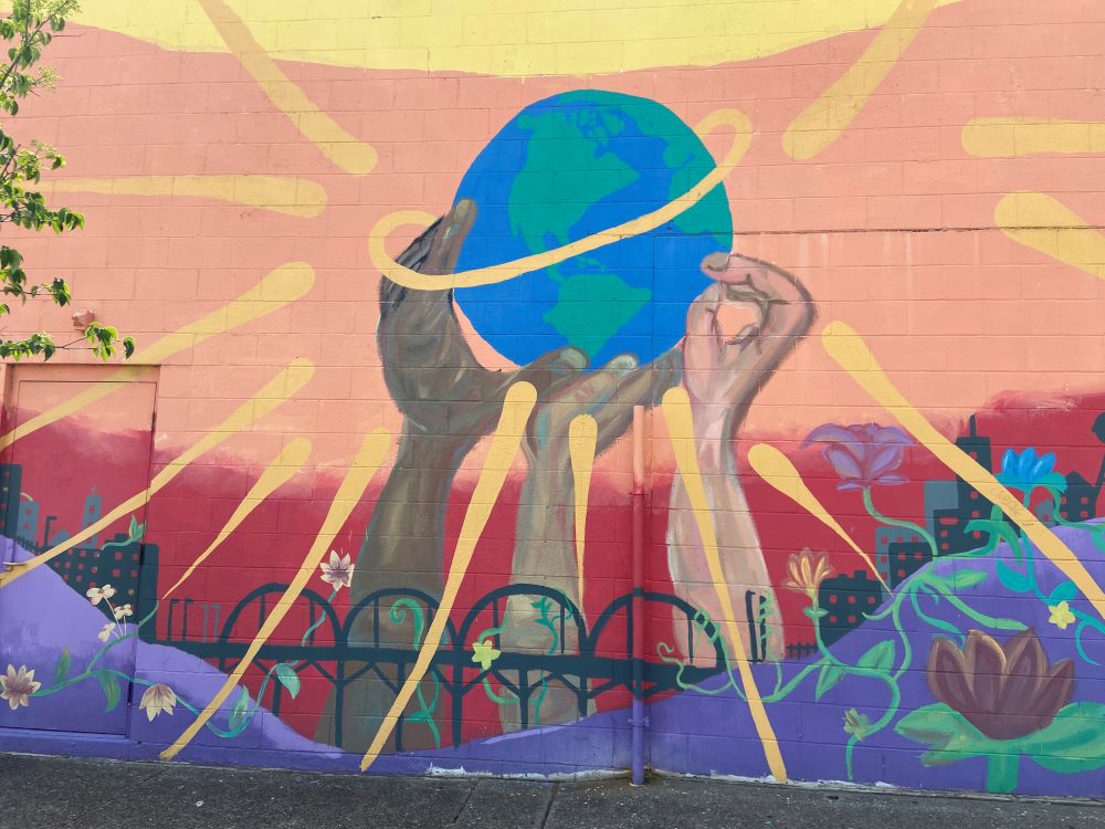 street art shows arms and hands of different colors holding up the earth