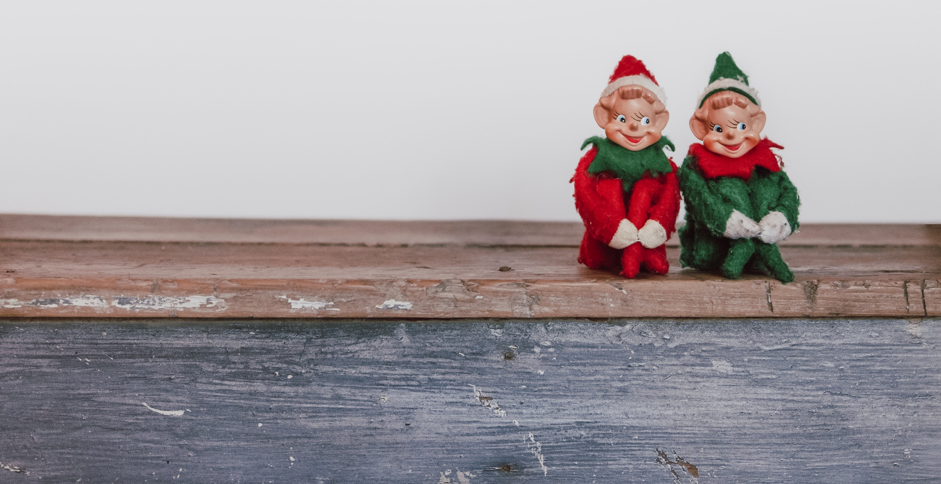Two small Santa elves sit on shelf.