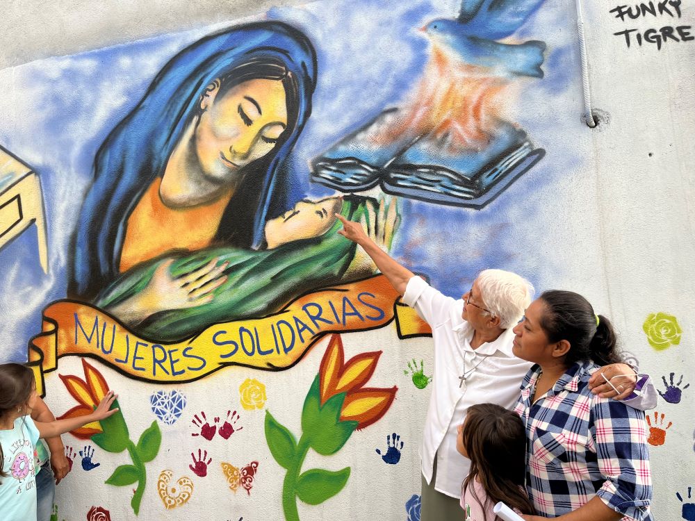 La hermana Del Servicio Social Virginia Bahena acompaña a una madre soltera de la comunidad a la que sirve en Nuevo Laredo, México, y muestra un colorido mural con imágenes religiosas.