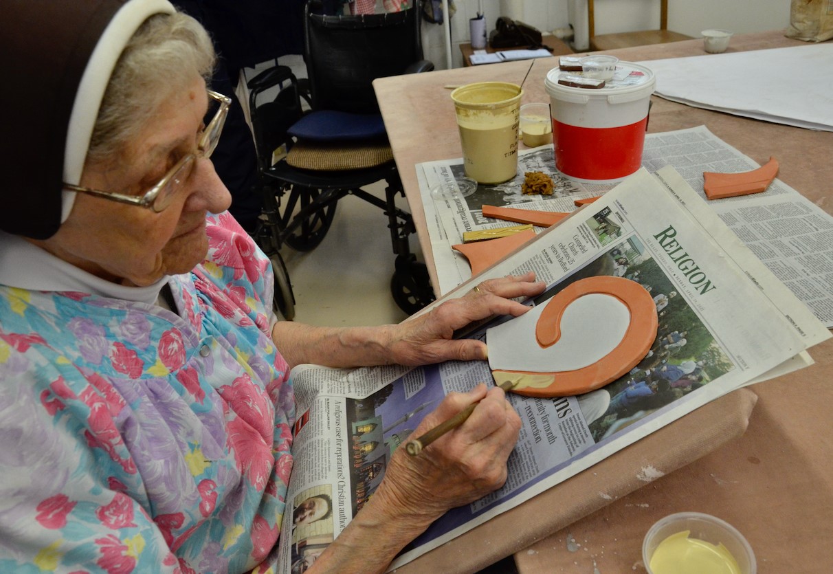 Sylvania Franciscan Sr. Jane Mary Sorosiak paints colored glaze onto a ceramic tile. When the painting is complete, the tile will be baked to harden the glaze into a permanent coating. (GSR photo/Dan Stockman)