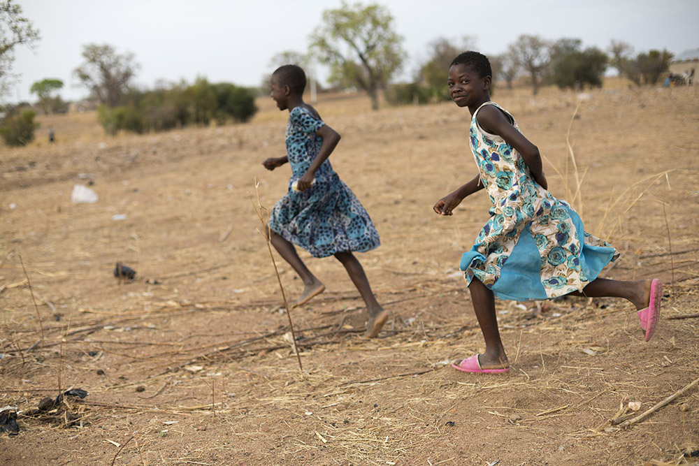 Children in Ghana run together through a dry field that has been severely affected by irregular weather patterns caused by climate change. (CNS/Courtesy of Catholic Relief Services/Jake Lyell)