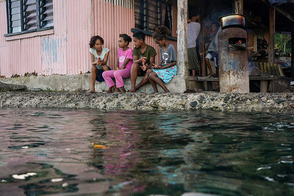Village children pass the time in front of a home next to a flooding sea wall at high tide in Serua Village, Fiji, July 15. As the community runs out of ways to adapt to the rising Pacific Ocean, the 80 villagers face the painful decision whether to move. (CNS/Reuters/Loren Elliott)