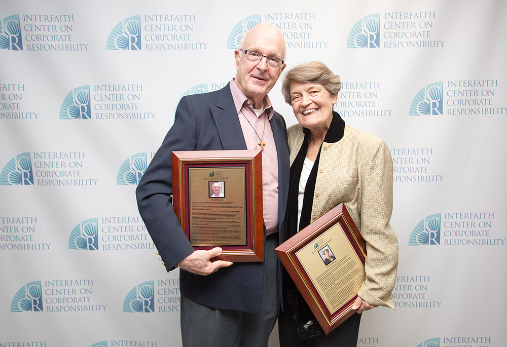 A white man and a white woman pose for a photo, both holding plaques
