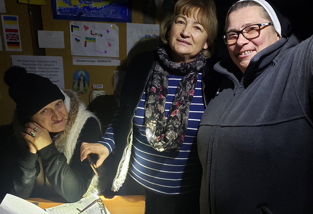 Dominican Sr. Mateusza Trynda, right, with volunteers at a darkened humanitarian center in Zhovkva, Ukraine, lit only by flashlights given electrical challenges. (GSR photo/Chris Herlinger)