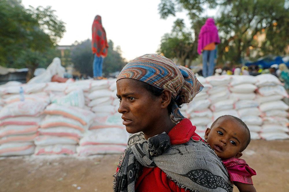 Una mujer lleva a un bebé mientras hace cola para conseguir comida en la escuela primaria de Tsehaye, convertida en refugio temporal para desplazados por el conflicto, en la ciudad de Shire, situada en la región etíope de Tigré, el 15 de marzo de 2021. (Foto: CNS/Reuters/Baz Ratner)