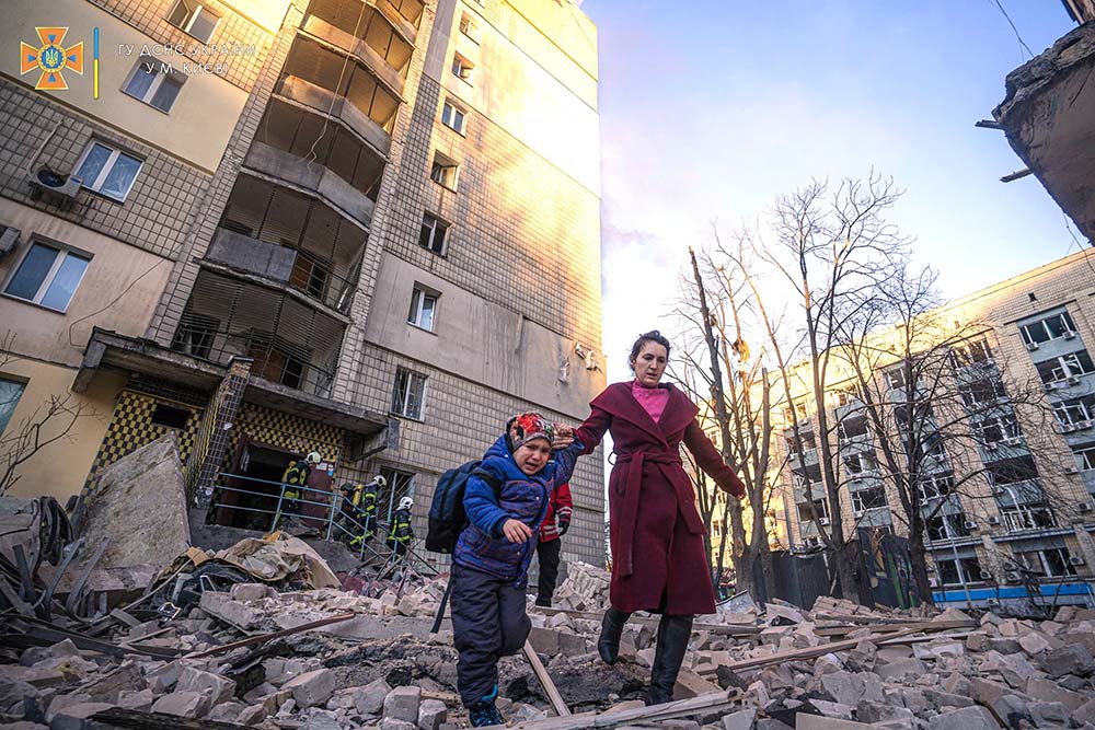 A woman with a child evacuates from a residential building damaged by Russian shelling in Kyiv, Ukraine, March 16. (CNS/State Emergency Service of Ukraine handout via Reuters)
