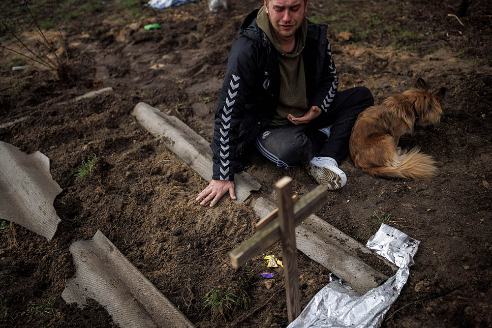 Serhii Lahovskyi, 26, mourns next to the grave of his friend Ihor Lytvynenko after Lytvynenko was found beside a building's basement in Bucha, Uraine, April 6. Residents say Russian soldiers killed Lytvynenko. (CNS/Reuters/Alkis Konstantinidis)