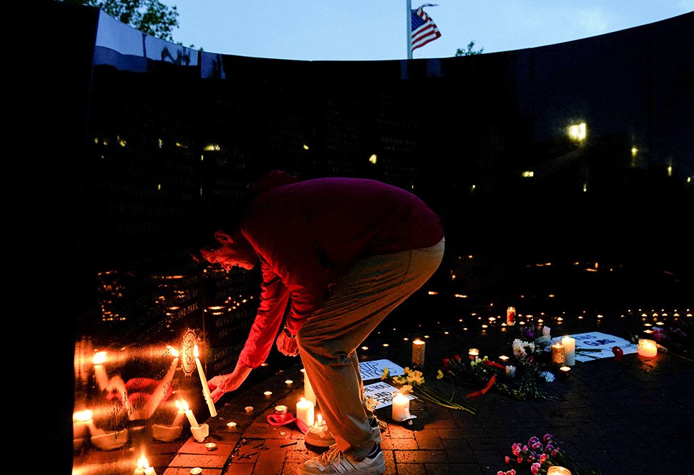 A person in the Chicago suburb of Highland Park, Illinois, lights a candle at a memorial site July 5 near the parade route the day after a mass shooting at a Fourth of July parade. Seven people were killed and dozens injured. (CNS/Reuters/Cheney Orr) A person in the Chicago suburb of Highland Park, Illinois, lights a candle at a memorial site July 5 near the parade route the day after a mass shooting at a Fourth of July parade. Seven people were killed and dozens injured. (CNS/Reuters/Cheney Orr)