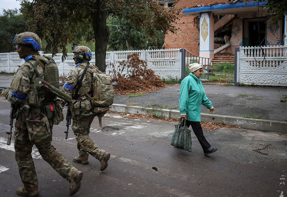 A woman passes Ukrainian servicemen patrolling an area Sept. 14 in Izium. (CNS/Reuters/Gleb Garanich)