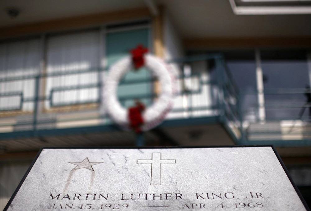 A white commemorative plaque in front of a motel with a wreath on a balcony