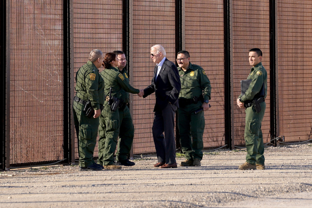Biden, wearing a suit and aviators, shakes a Border Patrol agents hand by the border fence