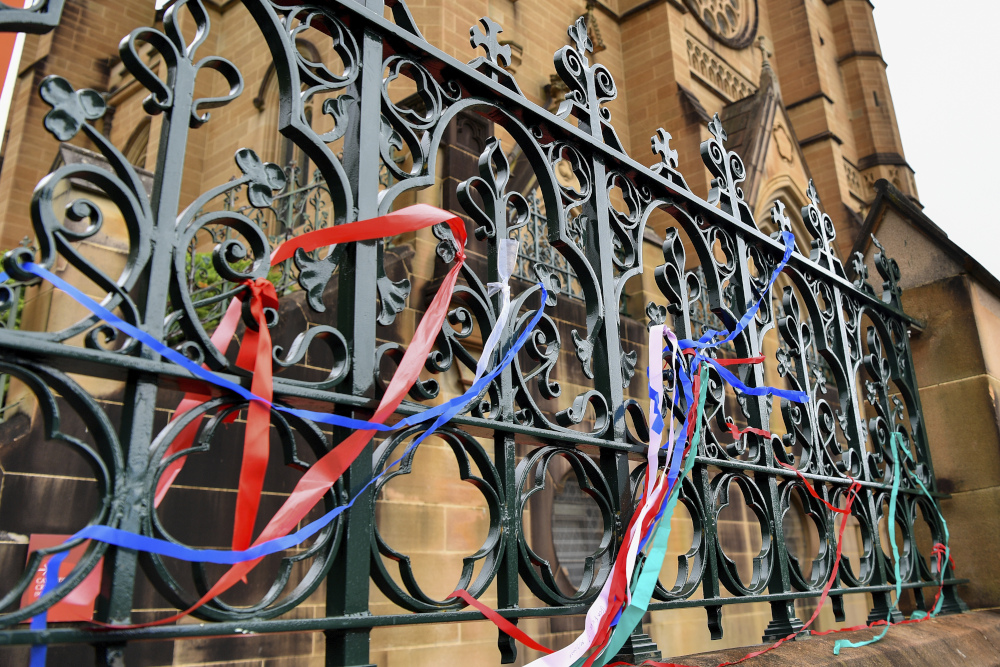 Long colorful ribbons are intertwined with the metal ornamentation of a fence outside a cathedral