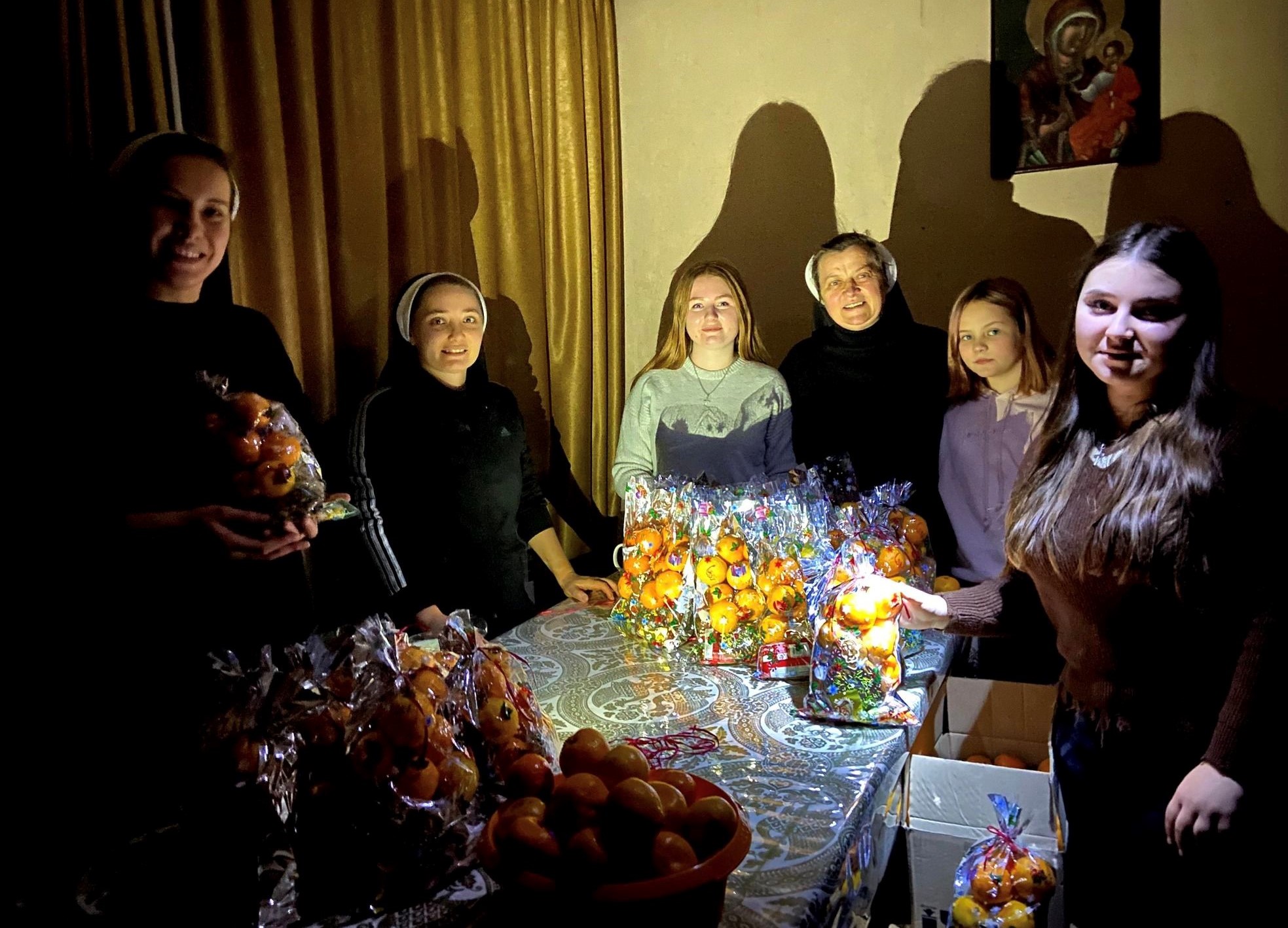 Basilian Sisters and young people prepare for St. Nicholas Day during a blackout in eastern Ukraine on Dec. 19, 2022, the feast of St. Nicholas. They are around a table with holiday food and they cast shadows on the walls.  calendar, which Ukraine follows. (