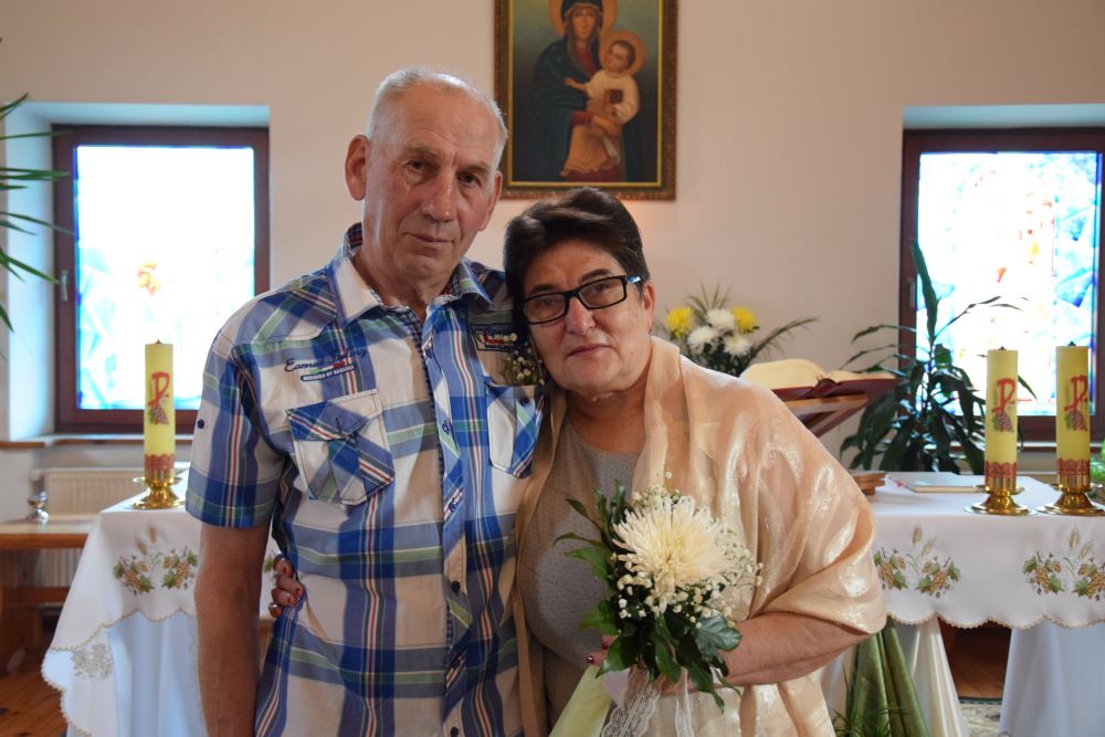 Viktoria and Vasyl Mytsensky stand together in front of an altar table. Viktoria wears a shawl and holds flowers.