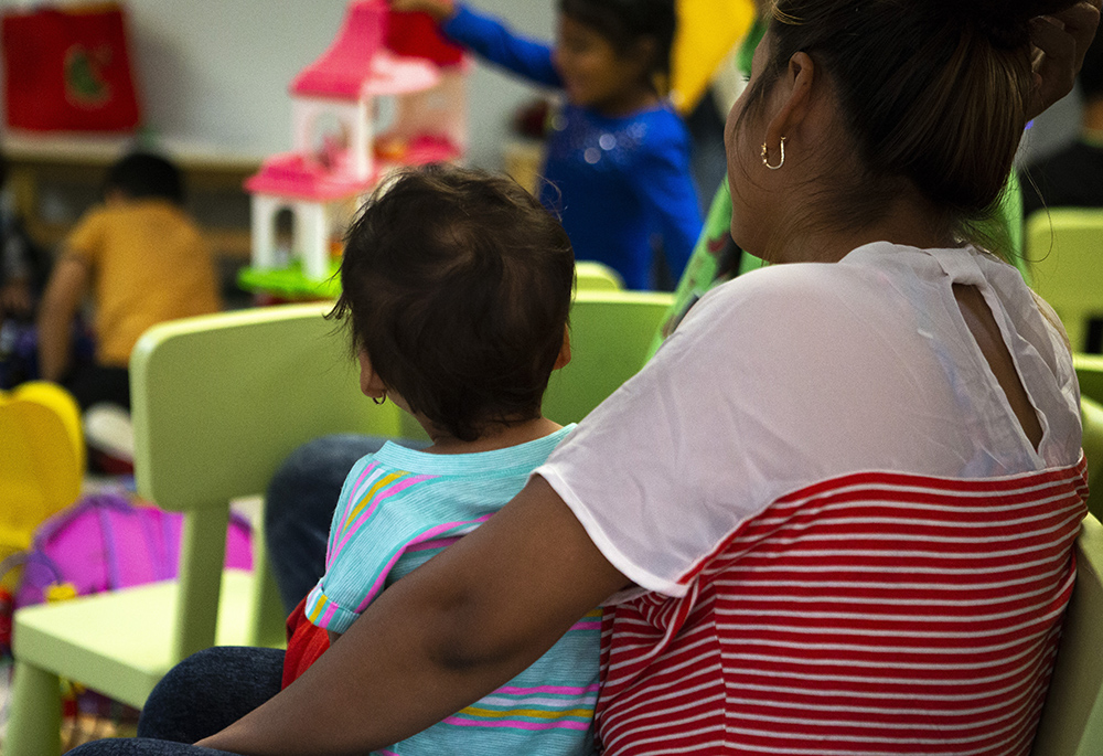 A Central American woman, who was recently released from U.S. custody, holds her child July 1, 2018, as they watch other immigrant children play at a Catholic Charities-run respite center in McAllen, Texas. (CNS/Chaz Muth)